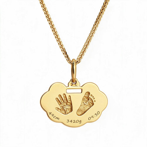 Gold-tone handprint and footprint pendant with sample birth details engraved along its lower edge.