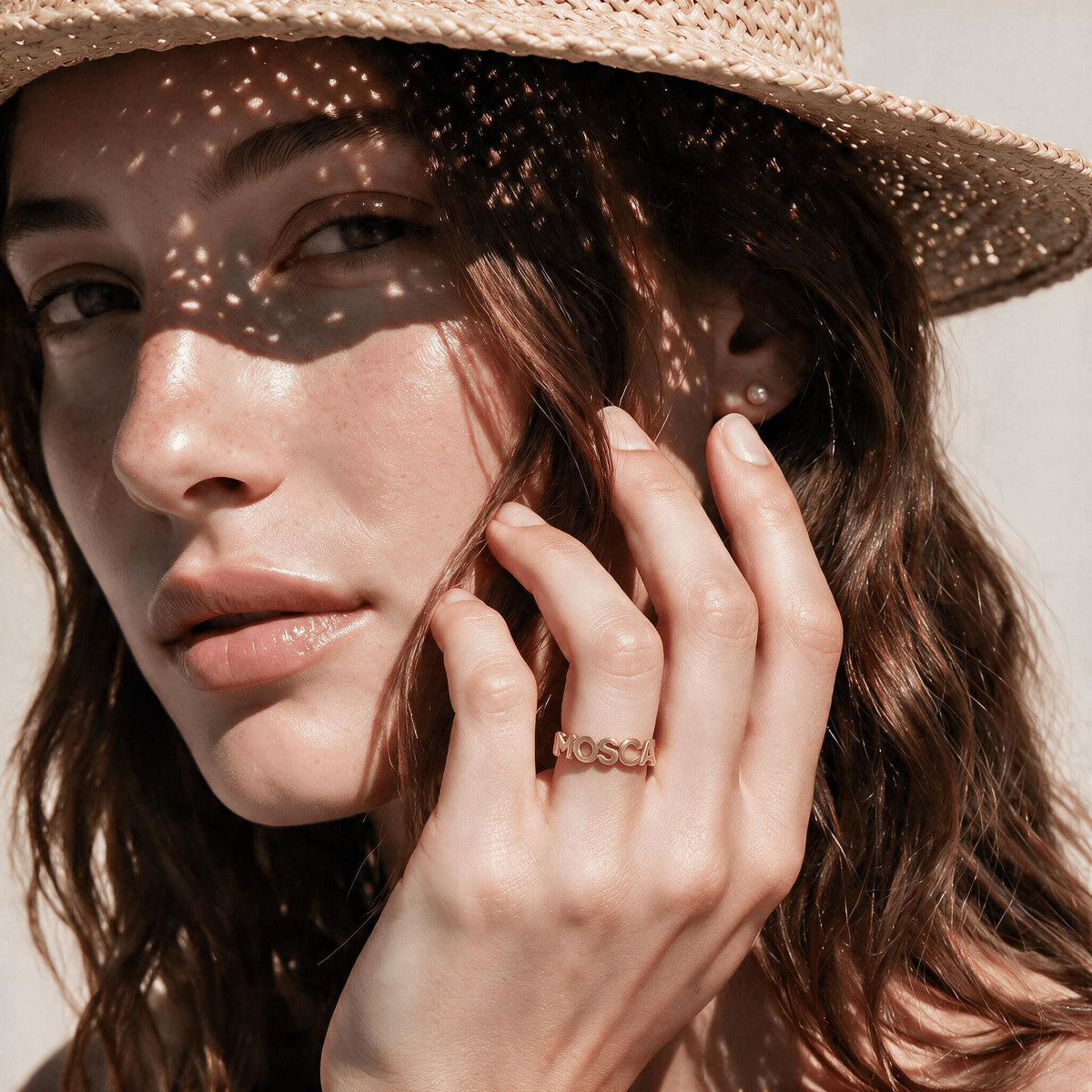 Woman wearing a gold-tone name loop ring with her hand resting against her face.