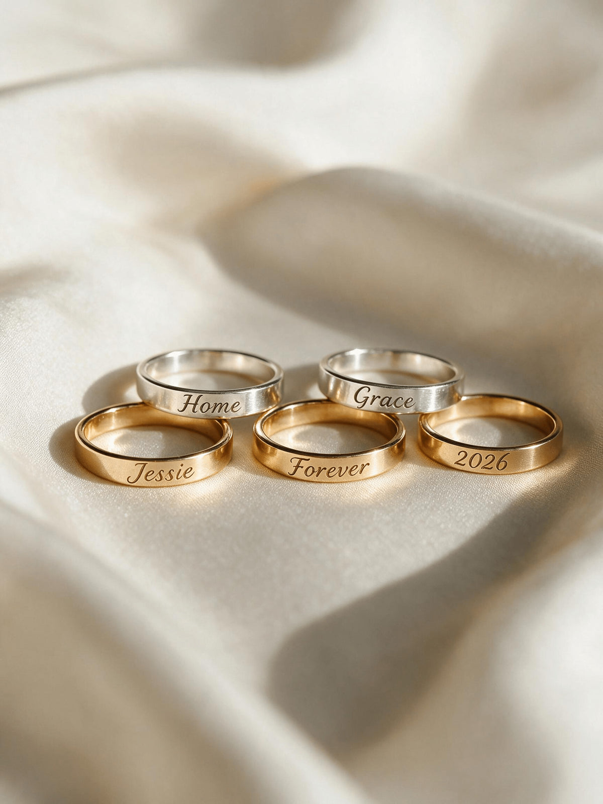Five engraved keepsake bands arranged on a light stone surface in warm sunlight.