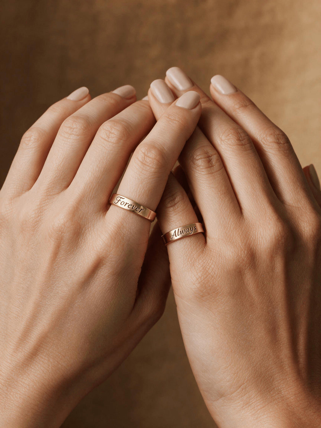 Hands wearing two gold-tone engraved keepsake bands.